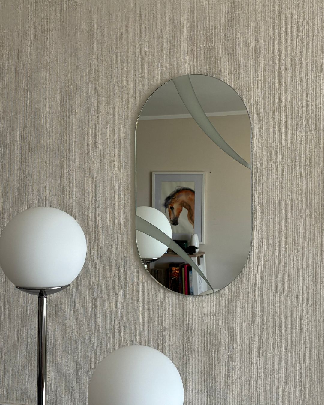 Espejo ovalado decorativo modelo Eclipse con franjas arenadas de precisión instalado en la pared de un living moderno. Destaca por sus curvas suaves y diseño de autor fabricado en Chile.