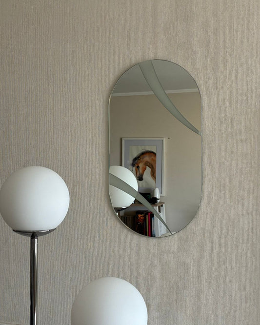 Espejo ovalado decorativo modelo Eclipse con franjas arenadas de precisión instalado en la pared de un living moderno. Destaca por sus curvas suaves y diseño de autor fabricado en Chile.